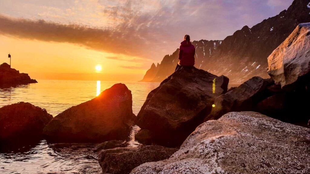 Woman sitting on rocks watching sunset over ocean