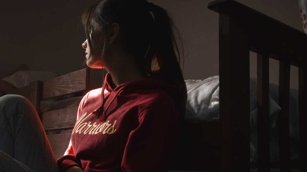 |Young girl looking very sad sitting on the floor by her bed