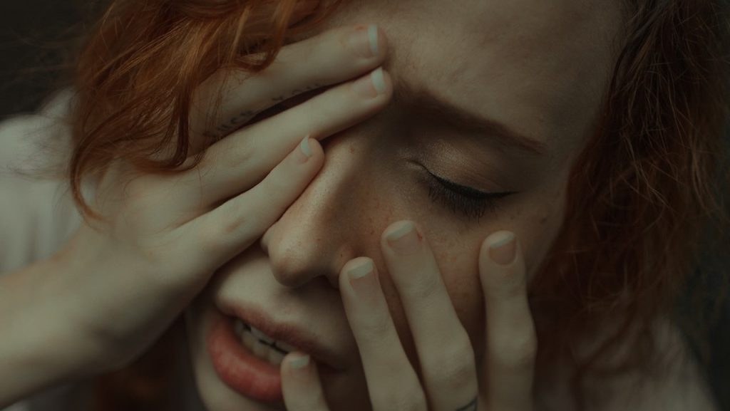 Distressed girl holding her hands up over her face.