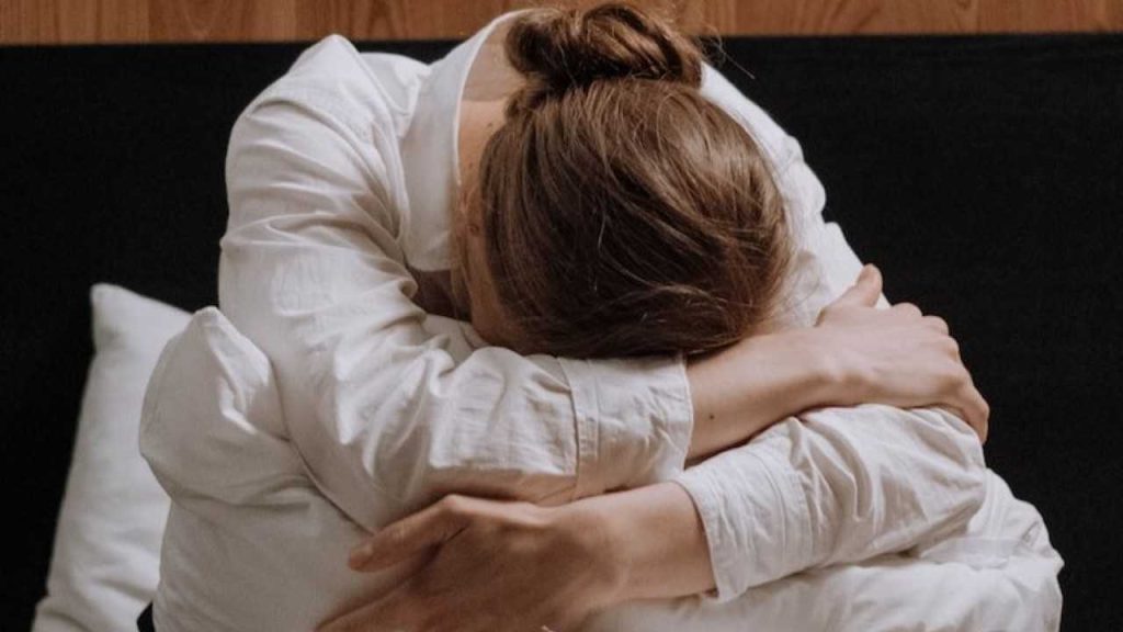 exhausted girl with her head on her knees sitting up in her bed.